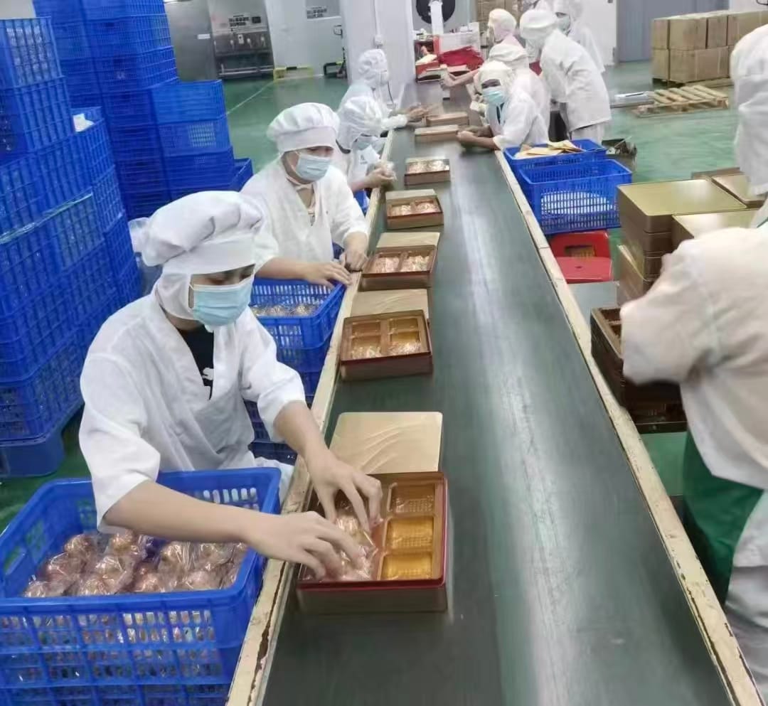 Manual food packaging process: a worker carefully placing packaged food into export cartons at a packing station, demonstrating quality control and attention to detail in the secondary packaging stage before international logistics.