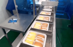 Automated food packaging line with conveyor system, efficiently processing pre-packed meal containers