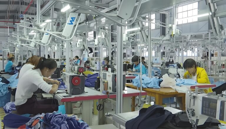 Manual garment folding process in a clothing factory, highlighting the labor-intensive workflow and space-consuming buffer zones