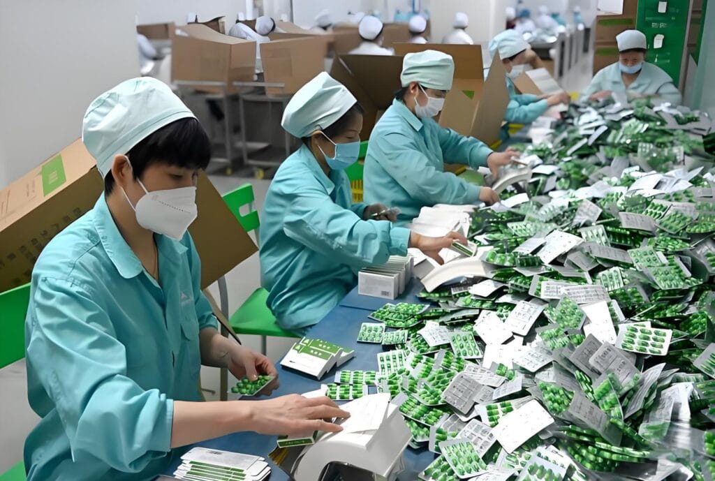 Manual pharmaceutical cartoning process: Workers manually loading blister packs of pills into cartons in a pharmaceutical manufacturing facility, highlighting the inefficiency of manual labor vs automated pharmaceutical cartoning machines.